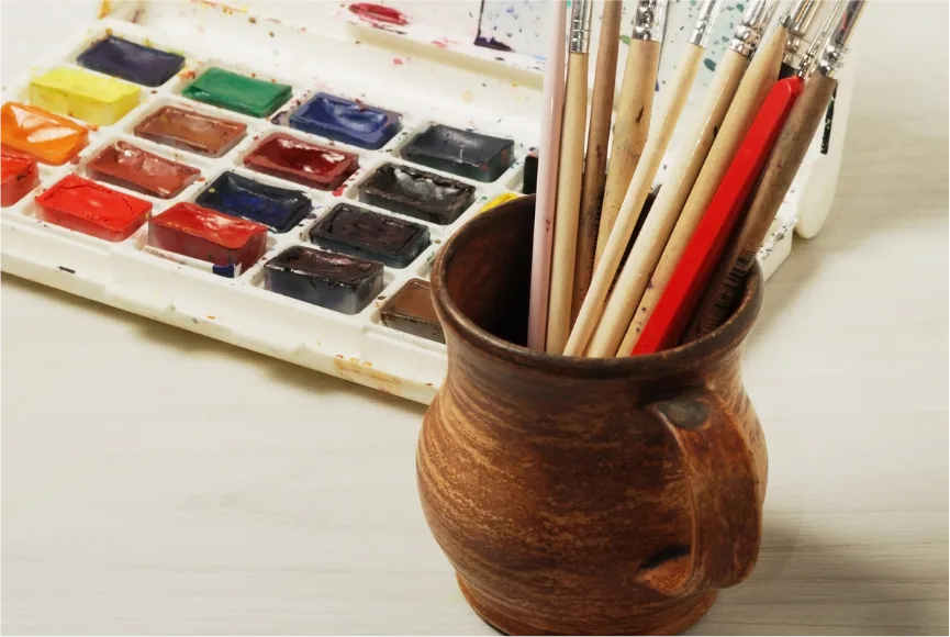 watercolor paint palette and watercolor brushes in a pottery mug