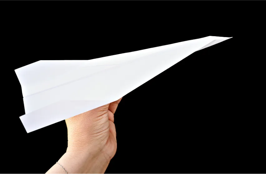 hand holding white paper airplane on black background